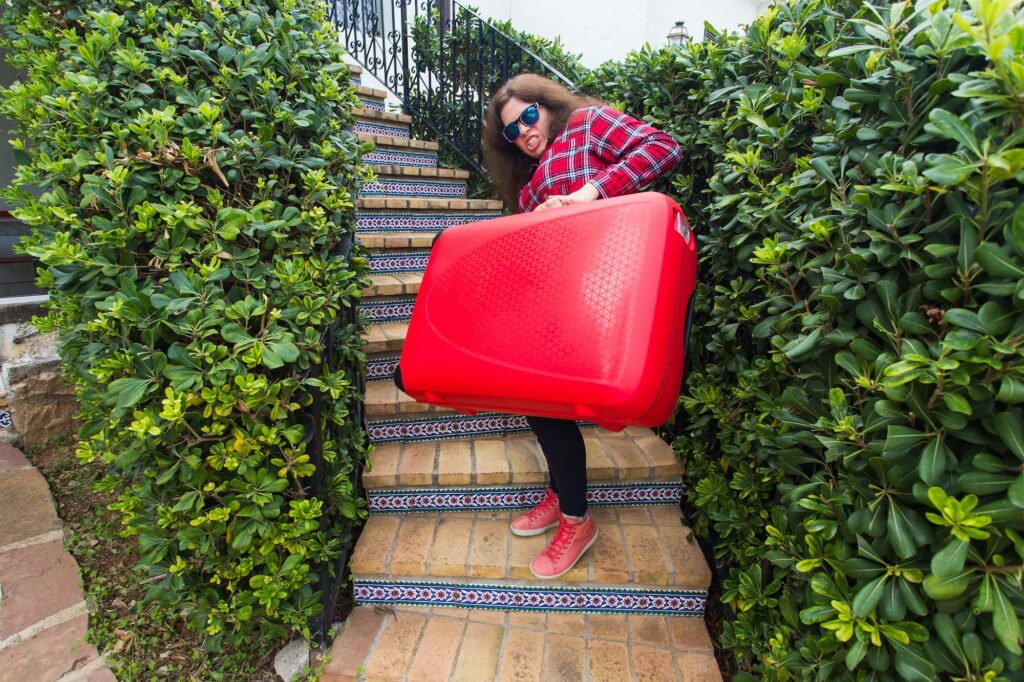 Holidays, travel, people concept - young woman with heavy red suitcase